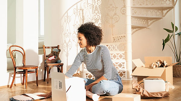 Lady wearing a black and white stripey top sitting cross legged on the floor surrounded by boxes and unpacking a Mondi MailerBag