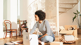 Lady wearing a black and white stripey top sitting cross legged on the floor surrounded by boxes and unpacking a Mondi MailerBag