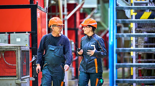 Two Mondi colleagues wearing protective equipment walking through a warehouse next to heavy machinery, engaged in conversation.