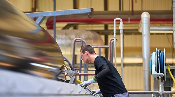 A man wearing a black jumper, grey gloves and yellow earplugs operating a paper machine in a factory setting.