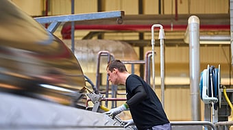 A man wearing a black jumper, grey gloves and yellow earplugs operating a paper machine in a factory setting.