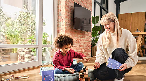 A woman and a child sitting together by a window while playing, with the woman holding a Mondi package.