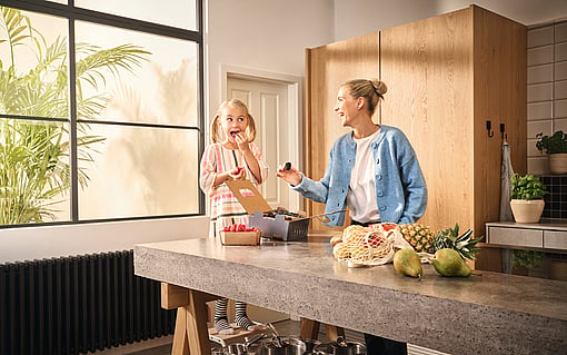 A woman and a child standing in a kitchen, laughing. On the kitchen counter, Mondi-branded corrugated packaging containing fresh fruit.