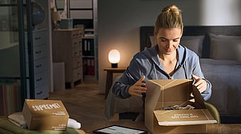 woman opening a package in a living room with other packages on the table next to her
