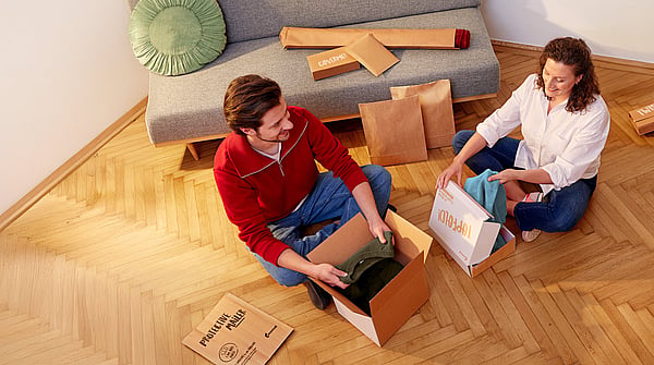 man and woman sitting cross legged opening corrugated packages