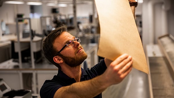 Male production worker wearing glasses and black t-shirt staring intently at a piece of packaging paper