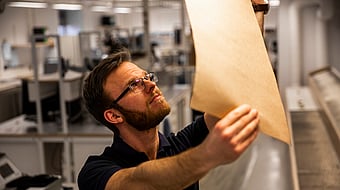 Male production worker wearing glasses and black t-shirt staring intently at a piece of packaging paper