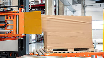 Automated stretch wrapping machine applying film around a palletized load in a warehouse.