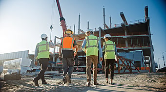 four workers on a construction site in wearing high-viz yellow and orange jackets