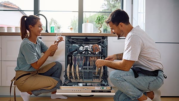 A man and a woman sitting next to a dish washer.