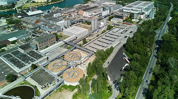 Aerial view of Mondi's Duino mill, located beside a canal and surrounded by green landscape.