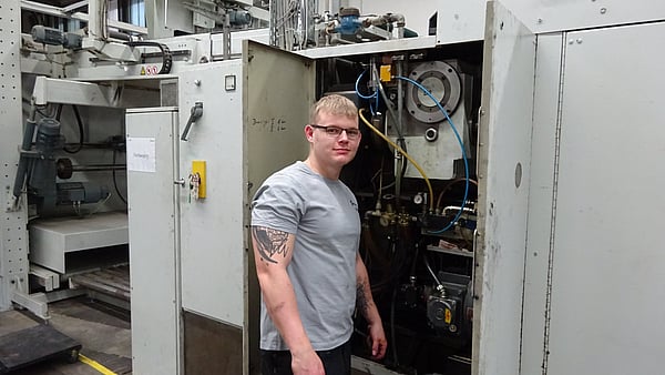 man in grey t-shirt and glasses stands next to an open cabinet in a factory setting