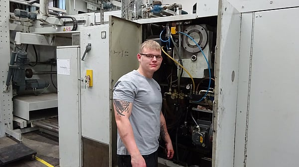 man in grey t-shirt and glasses stands next to an open cabinet in a factory setting