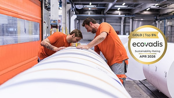 Two people in an industrial production hall inspect a large rolled material, with an EcoVadis Gold sustainability rating badge (Top 5%, April 2026) displayed on the image.