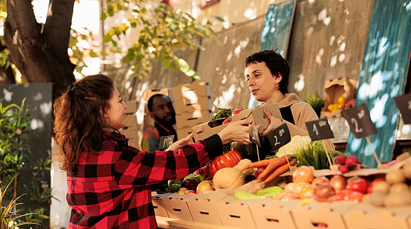 Women standing in front of selected fruit in corrugated boxes, buying fruit.