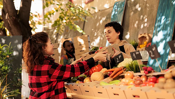 Women standing in front of selected fruit in corrugated boxes, buying fruit.