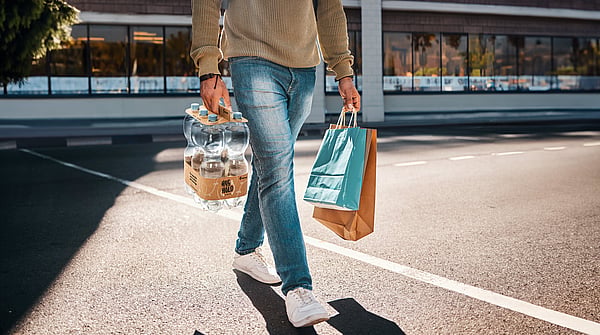 Hug&Hold, bottle bundle paper packaging being carried by a man wearing a beige jumper and blue jeans outside of a shop