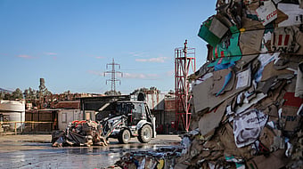 Tractor cleaning paper for recycling, with stacks of other paper materials visible in the background.