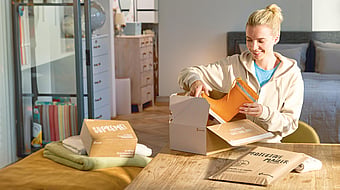 Woman sitting next to a table filled with Mondi packaging while unpacking a pair of rain boots.
