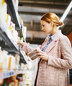 A woman is standing and selecting a product from a supermarket shelf.
