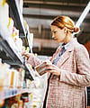 A woman is standing and selecting a product from a supermarket shelf.