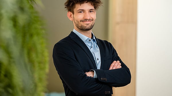 man in shirt and blazer standing cross armed and smiling at the camera