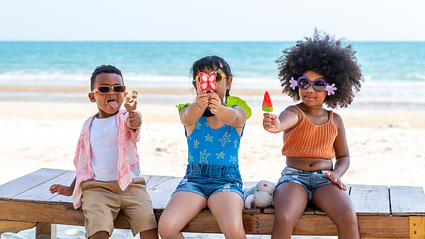 Three children at the beach in colourful clothing holding ice creams