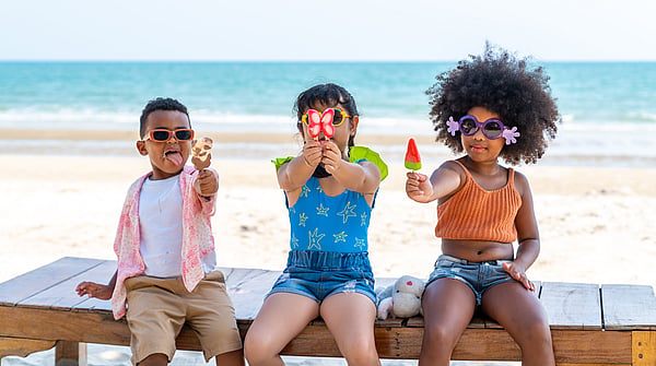 Three children at the beach in colourful clothing holding ice creams