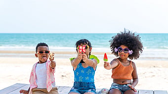 Three children at the beach in colourful clothing holding ice creams