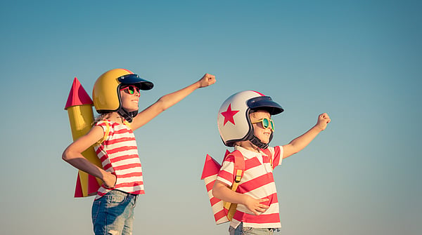 two children both wearing red and white stripey t-shirts and sunglasses dressed up as spacemen with their fists raised set against a blue sky