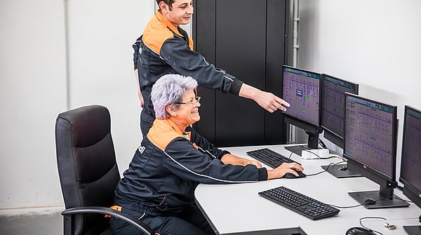 Senior female Mondi worker sits at a computer while a younger male colleague points to data on the screen.