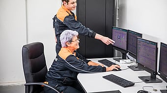 Senior female Mondi worker sits at a computer while a younger male colleague points to data on the screen.