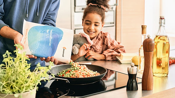 young girl sat at a kitchen table smiling and watching someone prepare food