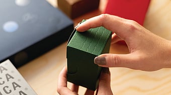 Photograph focusing on a woman’s hands opening a small premium packaging.