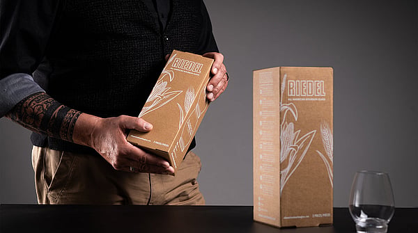 man in black clothing holding a brown corrugated box with a glass on the table next to him