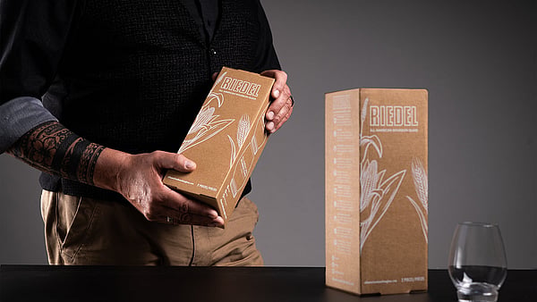 man in black clothing holding a brown corrugated box with a glass on the table next to him