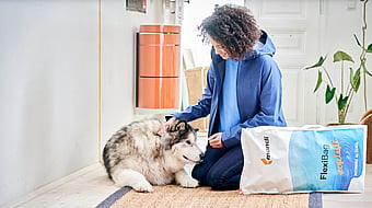 woman kneels down to pet a dog with packaging to her side