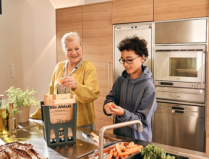 Two people preparing food together in a kitchen, with vegetables on a work surface.