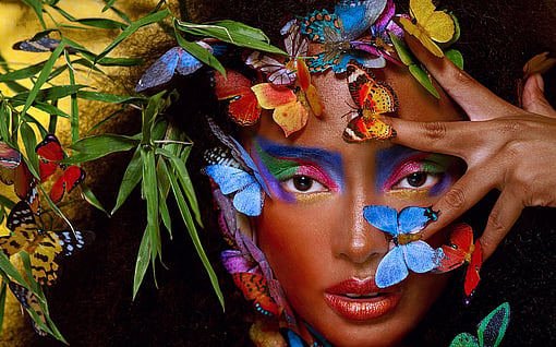 A woman is surrounded by colourful butterflies and staring at the camera.