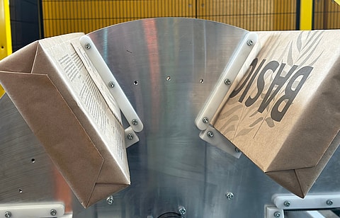 Paper bags moving through an industrial machine with a metal guiding mechanism during production.