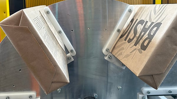 Paper bags moving through an industrial machine with a metal guiding mechanism during production.