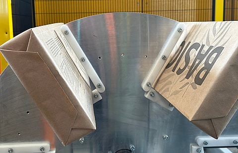 Paper bags moving through an industrial machine with a metal guiding mechanism during production.