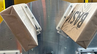 Paper bags moving through an industrial machine with a metal guiding mechanism during production.