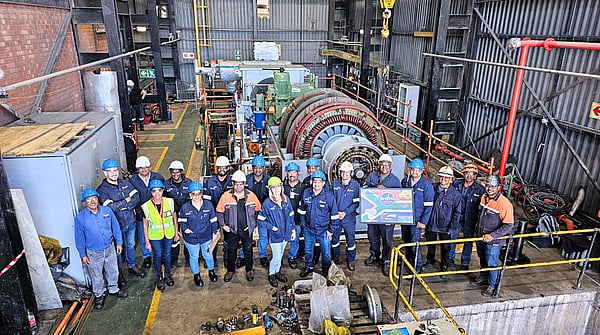 large group of people pose in front of factory machinery wearing hi-viz and blue jackets and hard hats