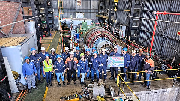 large group of people pose in front of factory machinery wearing hi-viz and blue jackets and hard hats