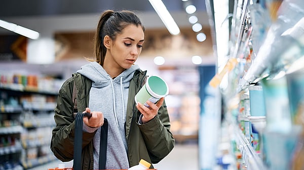 A young woman is reading a nutrition label while shopping.